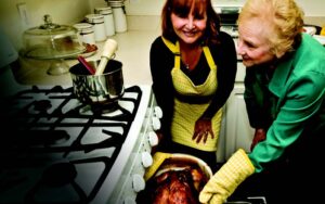 Grandmother & daughter pulling a turkey out of the oven.